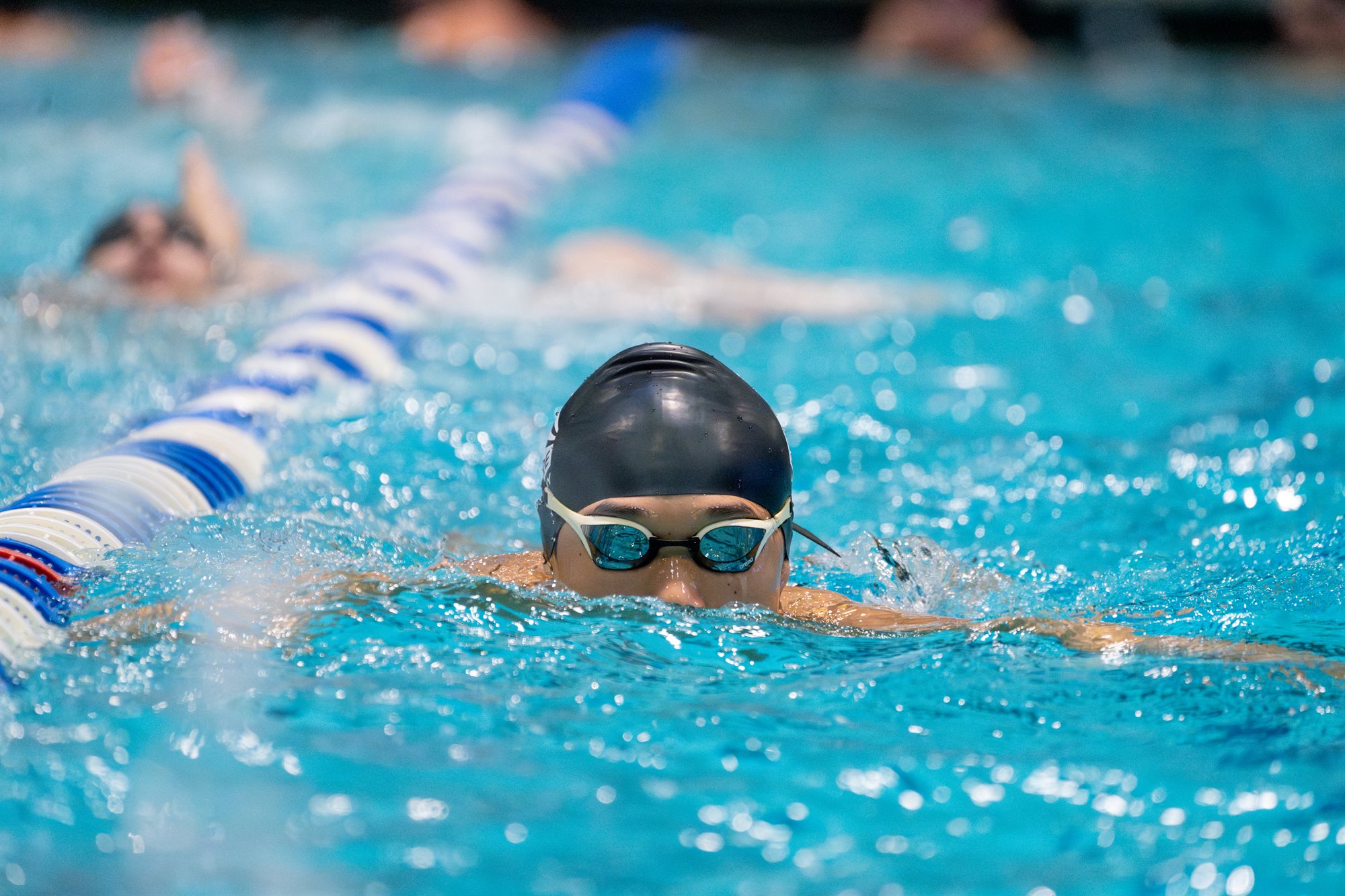 A swimmer facing forward in a pool lane, surrounded by blue water.
