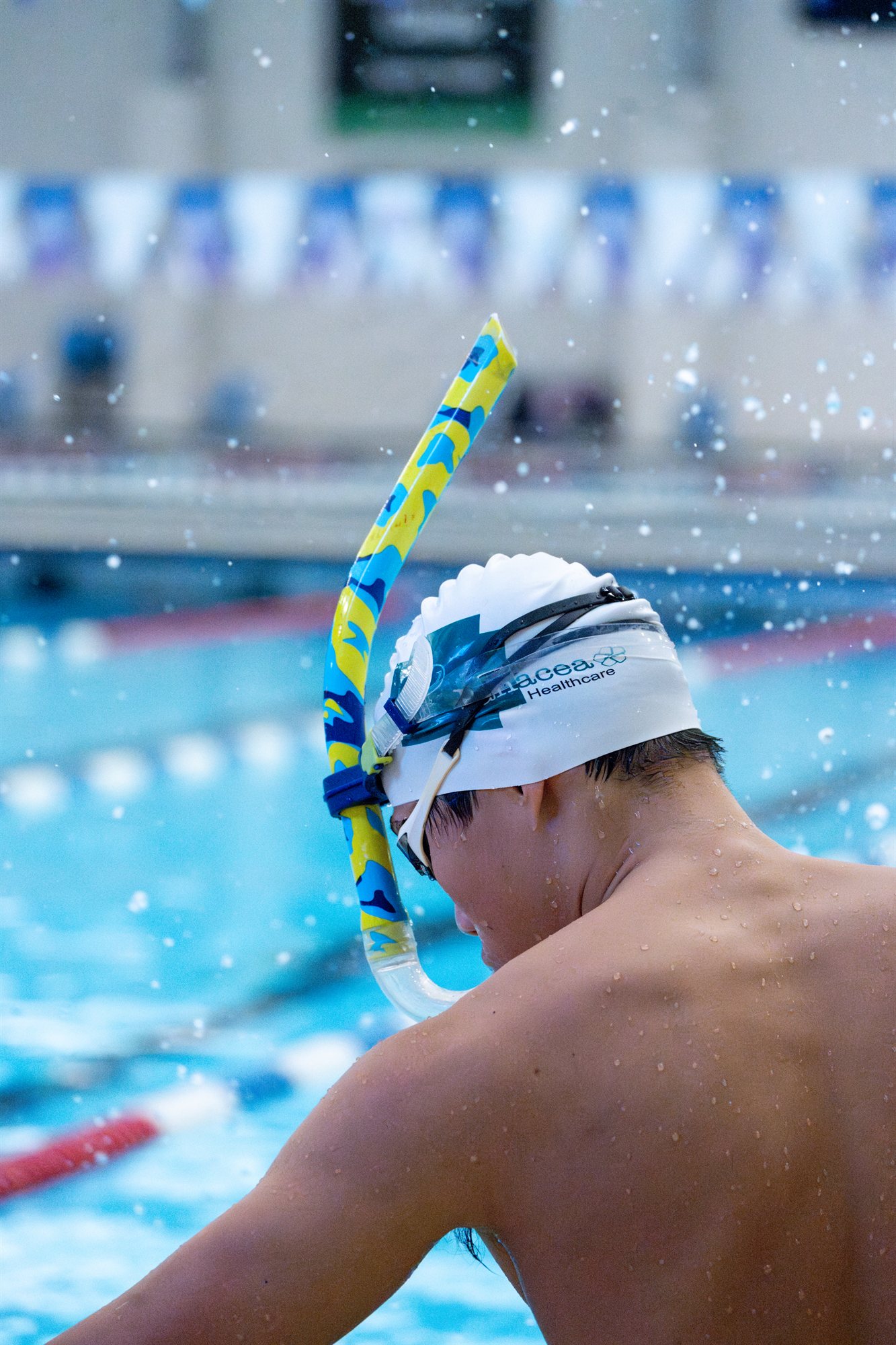 A swimmer poolside wearing a swimming cap, goggles and a snorkel.